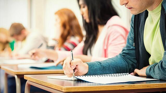 Mehrere Studierende sitzen an Tischen und arbeiten in ihren Unterlagen.