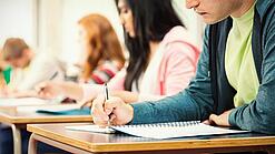 Mehrere Studierende sitzen an Tischen und arbeiten in ihren Unterlagen.