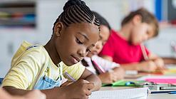 Grundschulkinder schreiben etwas in ihre Hefte.