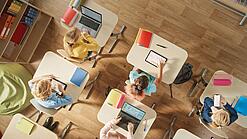 Kinder sitzen in einem Klassenzimmer und arbeiten mit verschiedenen digitalen Geräten.