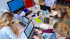 Vier junge Personen sitzen an einem Tisch. Auf dem Tisch stehen Laptops.