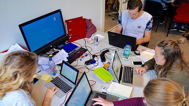 Vier junge Personen sitzen an einem Tisch. Auf dem Tisch stehen Laptops.