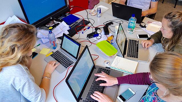 Vier junge Personen sitzen an einem Tisch. Auf dem Tisch stehen Laptops.