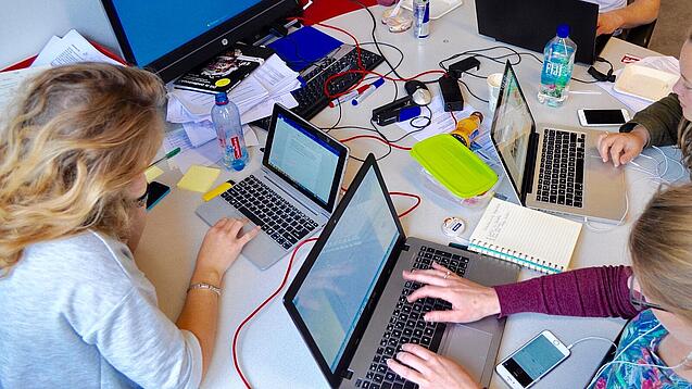Vier junge Personen sitzen an einem Tisch. Auf dem Tisch stehen Laptops.