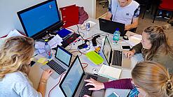 Vier junge Personen sitzen an einem Tisch. Auf dem Tisch stehen Laptops.