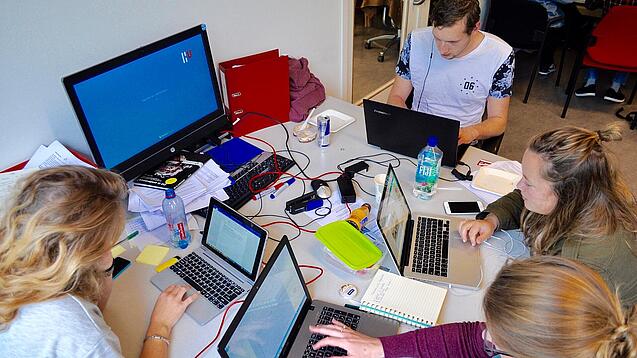 Vier junge Personen sitzen an einem Tisch. Auf dem Tisch stehen Laptops.