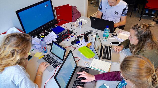Vier junge Personen sitzen an einem Tisch. Auf dem Tisch stehen Laptops.