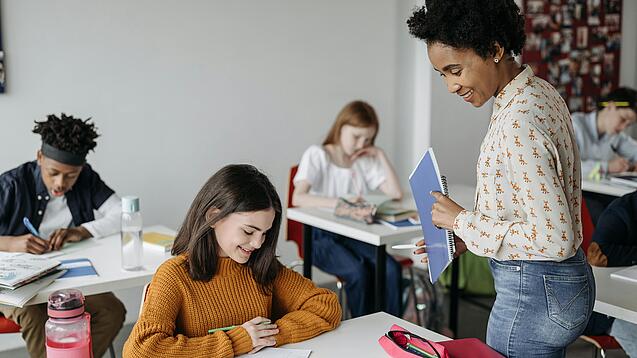Eine Lehrerin schaut einer Schülerin beim Lernen zu.