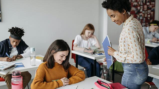 Eine Lehrerin schaut einer Schülerin beim Lernen zu.