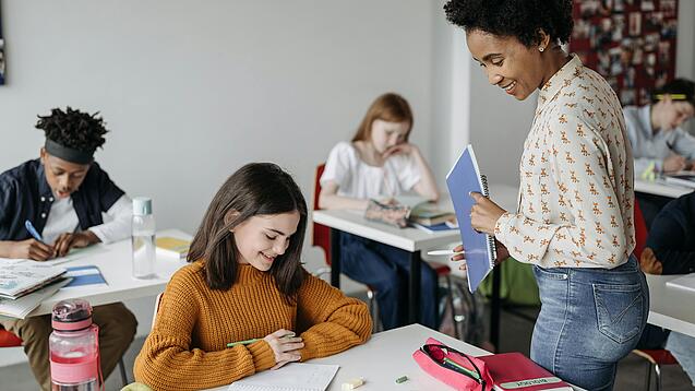 Eine Lehrerin schaut einer Schülerin beim Lernen zu.