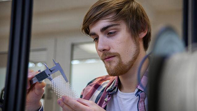 Junger Mann untersucht ein Objekt aus einem 3D-Drucker.