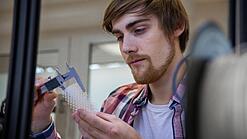 Junger Mann untersucht ein Objekt aus einem 3D-Drucker.