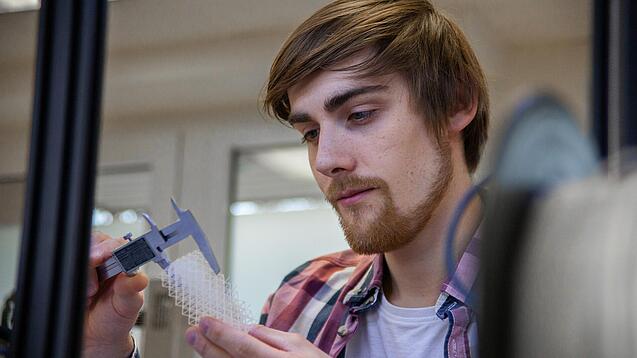 Junger Mann untersucht ein Objekt aus einem 3D-Drucker.
