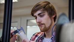 Junger Mann untersucht ein Objekt aus einem 3D-Drucker.