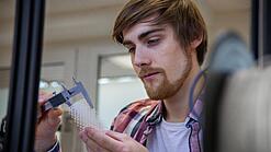 Junger Mann untersucht ein Objekt aus einem 3D-Drucker.