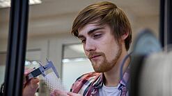 Junger Mann untersucht ein Objekt aus einem 3D-Drucker.