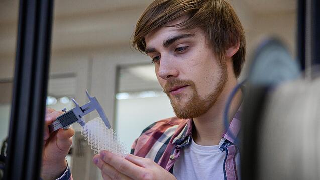 Junger Mann untersucht ein Objekt aus einem 3D-Drucker.