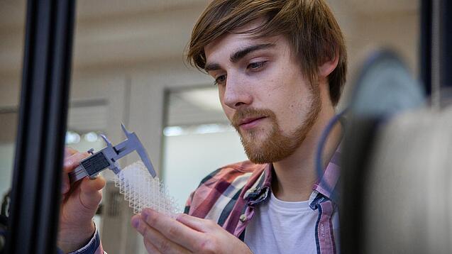 Junger Mann untersucht ein Objekt aus einem 3D-Drucker.