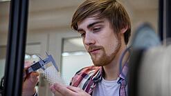 Junger Mann untersucht ein Objekt aus einem 3D-Drucker.