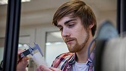 Junger Mann untersucht ein Objekt aus einem 3D-Drucker.