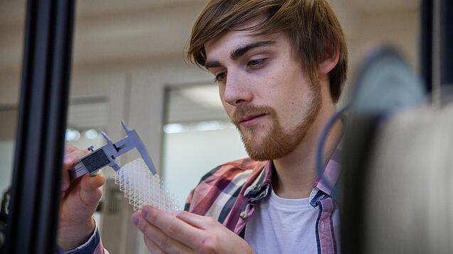 Junger Mann untersucht ein Objekt aus einem 3D-Drucker.