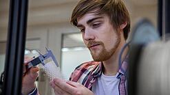 Junger Mann untersucht ein Objekt aus einem 3D-Drucker.