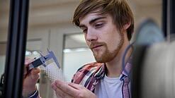 Junger Mann untersucht ein Objekt aus einem 3D-Drucker.