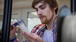 Junger Mann untersucht ein Objekt aus einem 3D-Drucker.