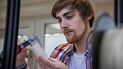 Junger Mann untersucht ein Objekt aus einem 3D-Drucker.