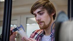 Junger Mann untersucht ein Objekt aus einem 3D-Drucker.