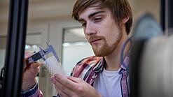 Junger Mann untersucht ein Objekt aus einem 3D-Drucker.