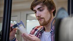 Junger Mann untersucht ein Objekt aus einem 3D-Drucker.