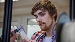 Junger Mann untersucht ein Objekt aus einem 3D-Drucker.