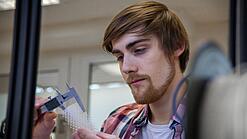 Junger Mann untersucht ein Objekt aus einem 3D-Drucker.