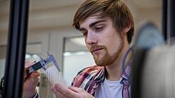 Junger Mann untersucht ein Objekt aus einem 3D-Drucker.