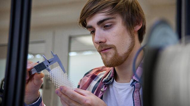 Junger Mann untersucht ein Objekt aus einem 3D-Drucker.
