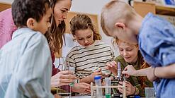 Mehrere Kinder und eine Lehrerin beugen sich über ein Mikroskop.