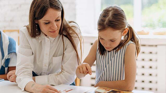 Eine Frau und ein Schulkind lesen gemeinsam ein Buch.