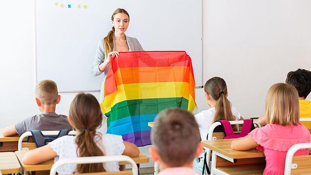 Eine Lehrerin zeigt einer Klasse eine Regenbogen-Fahne.