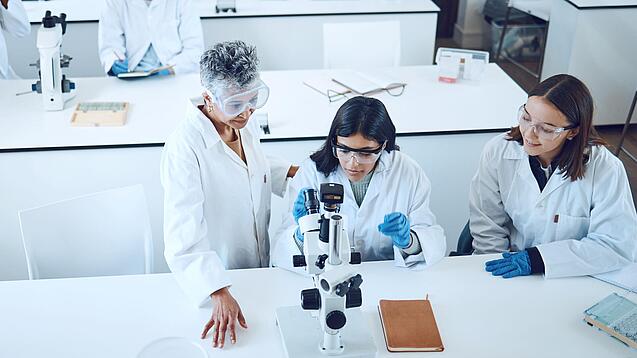 Gruppe Studierender und eine Dozentin in einem Chemiehörsaal vor Mikroskopen