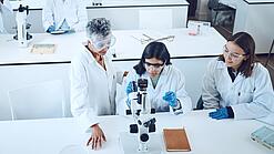Gruppe Studierender und eine Dozentin in einem Chemiehörsaal vor Mikroskopen