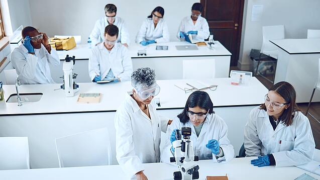 Gruppe Studierender und eine Dozentin in einem Chemiehörsaal vor Mikroskopen