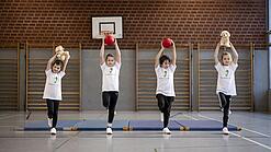 Vier Kinder turnen mit einem Ball.