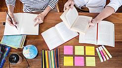 Schreibtisch mit Notizbüchern, Stiften und Textmarkern in Vogelperspektive.