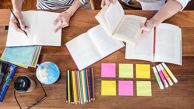 Schreibtisch mit Notizbüchern, Stiften und Textmarkern in Vogelperspektive.