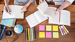 Schreibtisch mit Notizbüchern, Stiften und Textmarkern in Vogelperspektive.