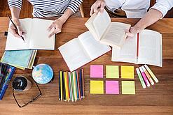 Schreibtisch mit Notizbüchern, Stiften und Textmarkern in Vogelperspektive.