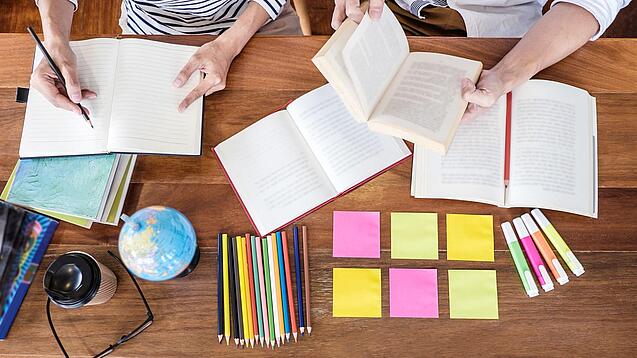 Schreibtisch mit Notizbüchern, Stiften und Textmarkern in Vogelperspektive.