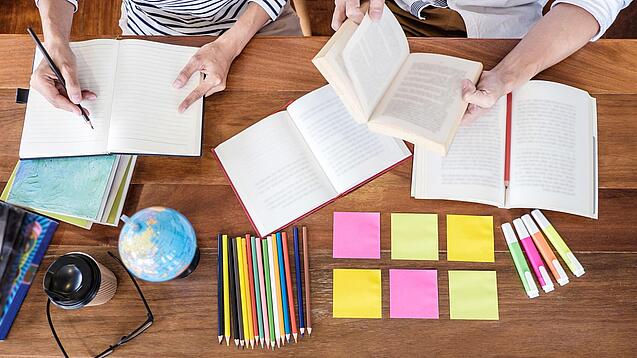 Schreibtisch mit Notizbüchern, Stiften und Textmarkern in Vogelperspektive.