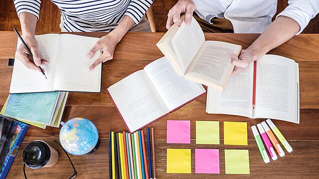 Schreibtisch mit Notizbüchern, Stiften und Textmarkern in Vogelperspektive.